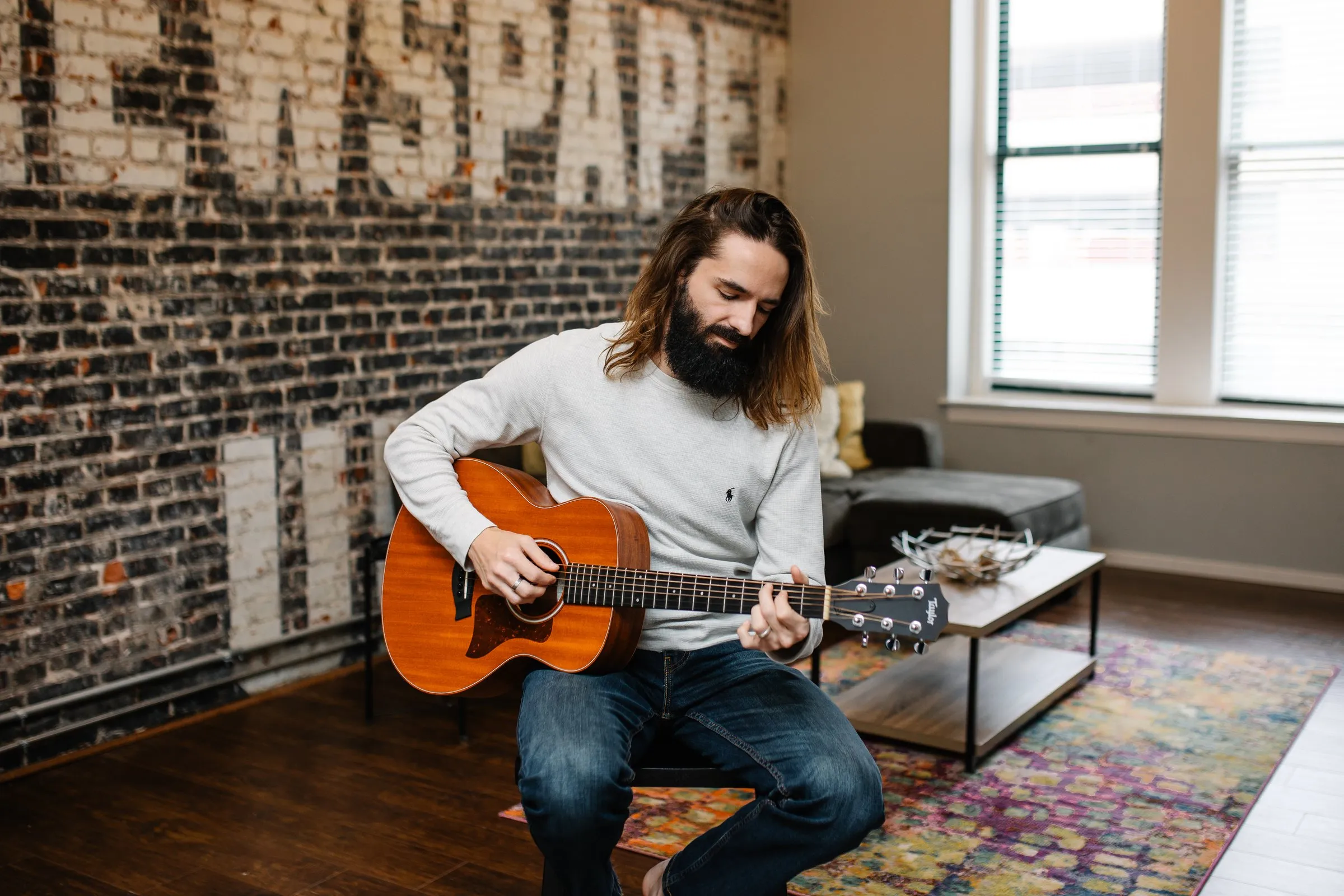 Borin playing acoustic guitar in a brick-walled loft
